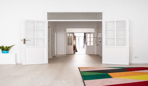 open white glazed doors leading into a hallway with a colourful carpet and a plant in a blue pot surrounding them